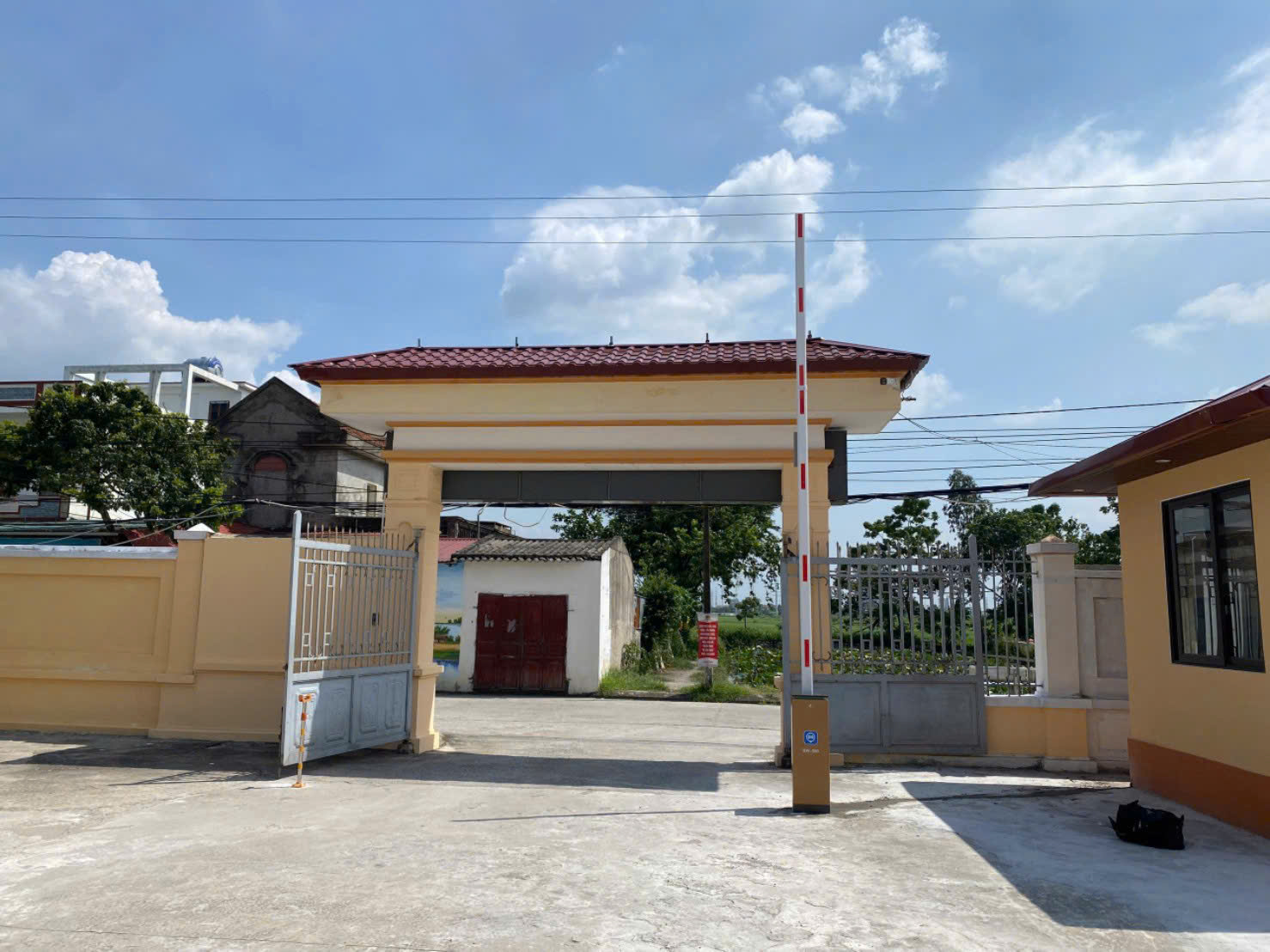 Cổng cơ quan lắp barrier tự động màu vàng đỏ giữa sân bê tông trời nắng